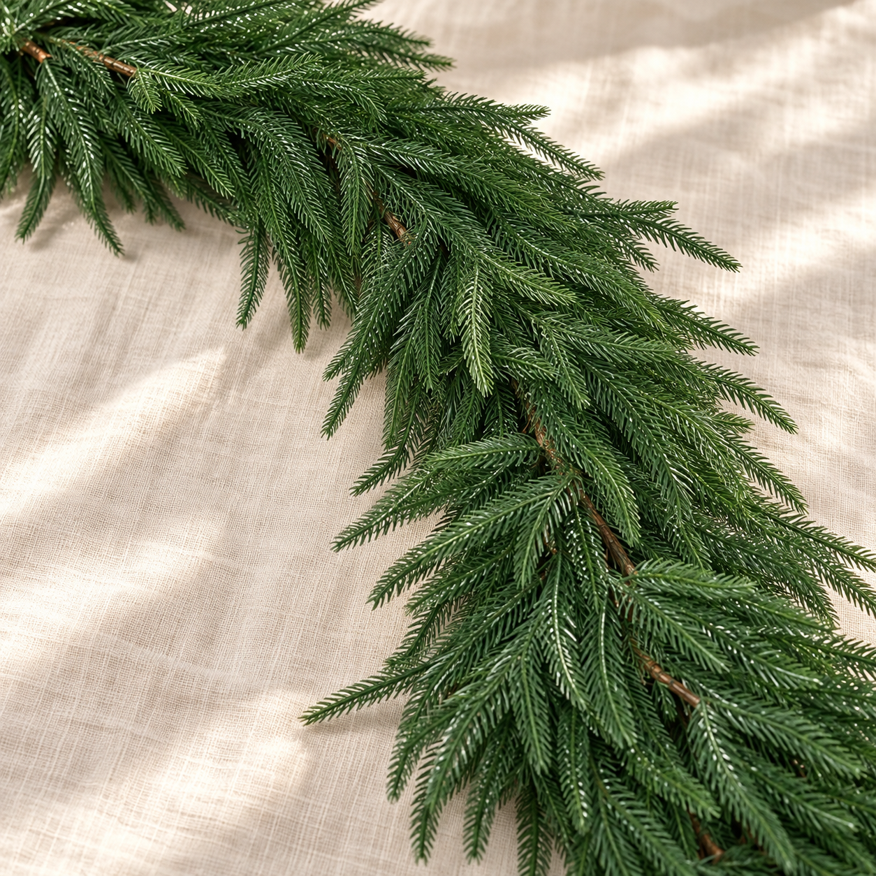 Close-up styling image of the Norfolk pine garland foliage on ivory linen. AI-generated product styling image based on the original Amazon product image; accessories shown are styling props.
